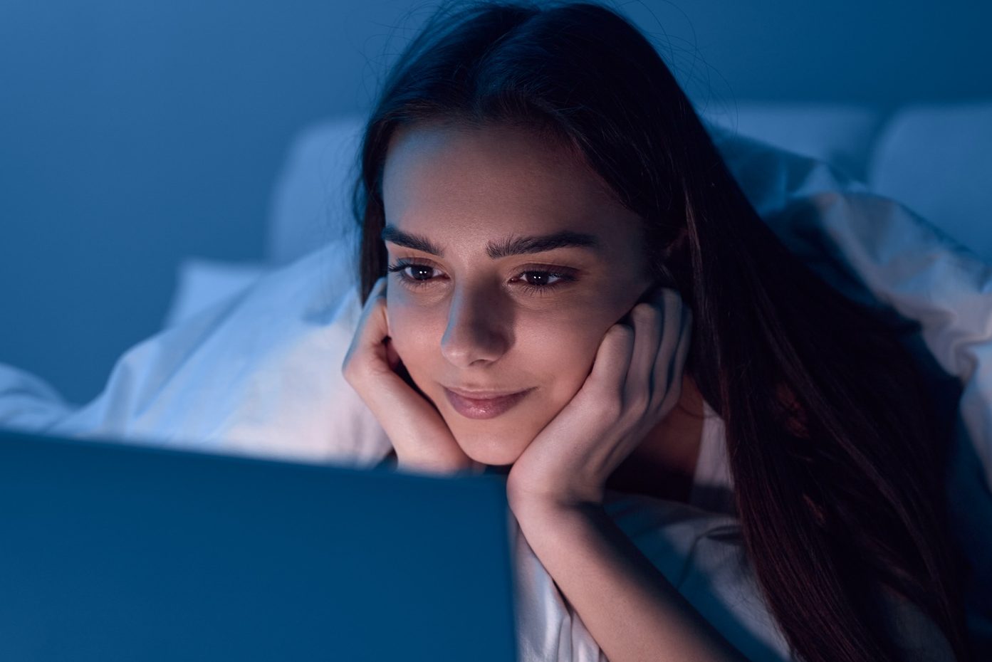Young Hispanic lady watching video on laptop while resting on bed